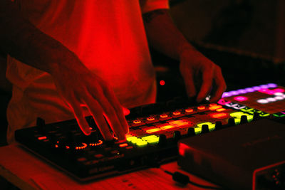 Guy hands covered by a red light using a coloured electronic synthesizer while in a moody  dark room