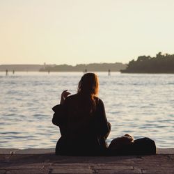 Rear view of woman sitting by sea against clear sky