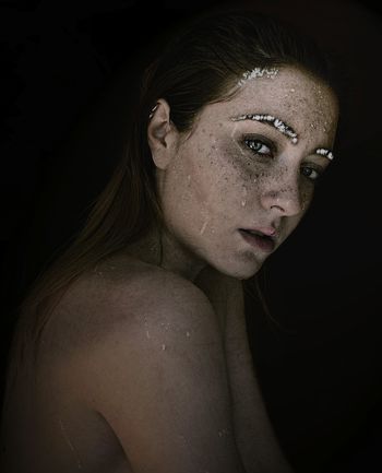 Close-up portrait of young woman against black background