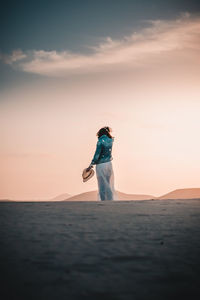 Woman standing on sand in desert against sky during sunset