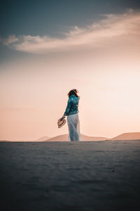 Woman standing by sea against sky during sunset