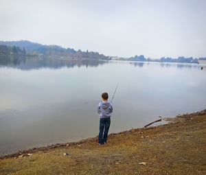 Rear view of boy fishing while standing on lakeshore