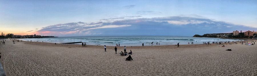 Panoramic view of people at beach against sky during sunset