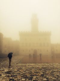 Man with umbrella standing by cathedral during foggy weather