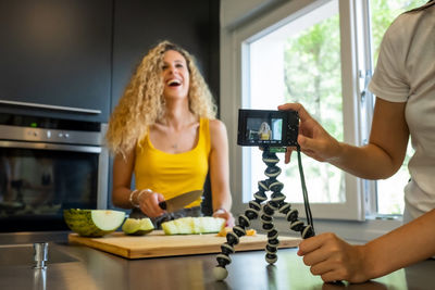 Midsection of woman filming friend cutting fruit