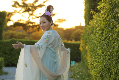 Portrait of beautiful woman with arms outstretched looking over shoulder in garden