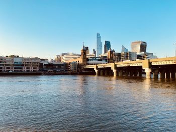 Bridge over river by buildings against clear sky