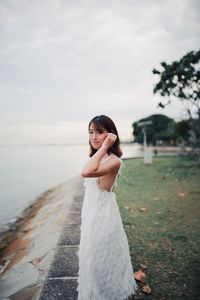 Young woman standing on field by sea against sky