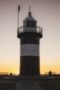 Lighthouse by sea against sky during sunset
