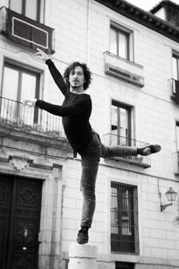 Low angle portrait of man dancing on bollard against building