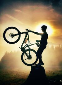 Silhouette man riding bicycle against sky during sunset