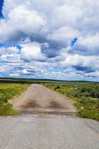 Road passing through field against cloudy sky