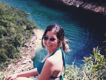 Portrait of happy woman sitting on hill against river during sunny day