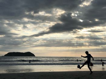 Silhouette boy on beach against sky during sunset