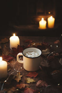 Cup of coffee with marshmallows on dark background with candle light