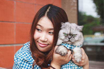 Close-up of thoughtful young woman holding cat against brick wall