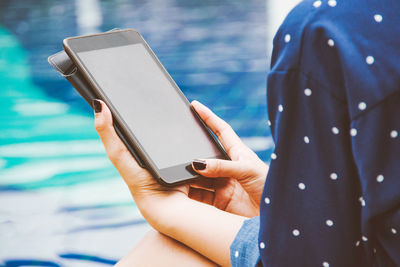 Cropped hands of woman using digital tablet while sitting at poolside