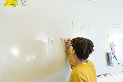 Boy writing on whiteboard in classroom