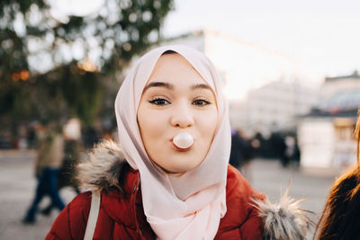 Portrait of young muslim woman blowing bubble gum in city