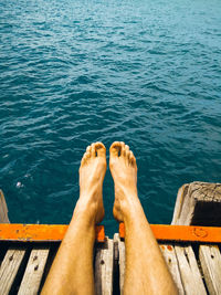 Low section of man relaxing on pier over sea