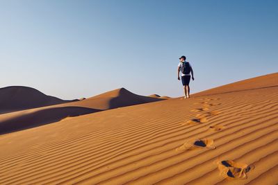 Man on sand dune in desert against sky