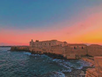 Built structure on sea against sky during sunset