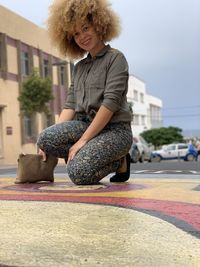 Portrait of smiling young woman sitting on sidewalk in city