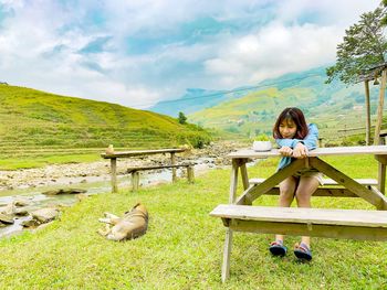 Woman sitting on grass against mountains against sky