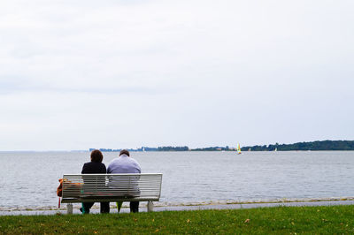 Rear view of man sitting on bench in calm lake