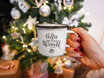 Cropped hand holding cup against christmas tree