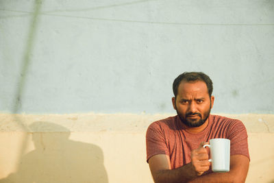 Portrait of man holding coffee cup against wall