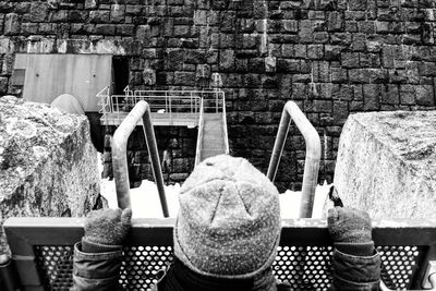 Rear view of boy standing by fence against brick wall during winter