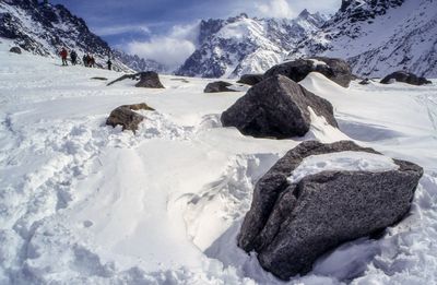 Rocks on snow covered field by mountains against sky