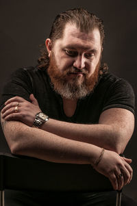 Bearded man sitting on chair against black background