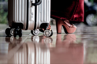 Low section of woman with suitcase standing on tiled floor