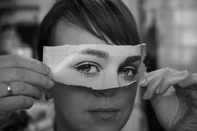 Close-up of woman holding torn paper eyes over face