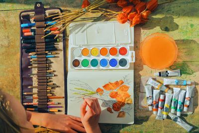 Cropped image of female artist painting flowers in notebook