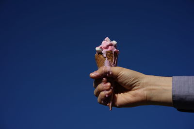Cropped hand holding ice cream cone against clear blue sky