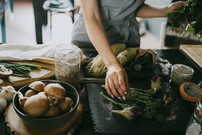 Female chef arranging broccolini and aubergines on slate at counter in studio kitchen