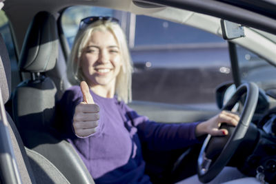 Portrait of smiling woman gesturing thumbs up sign while sitting in car