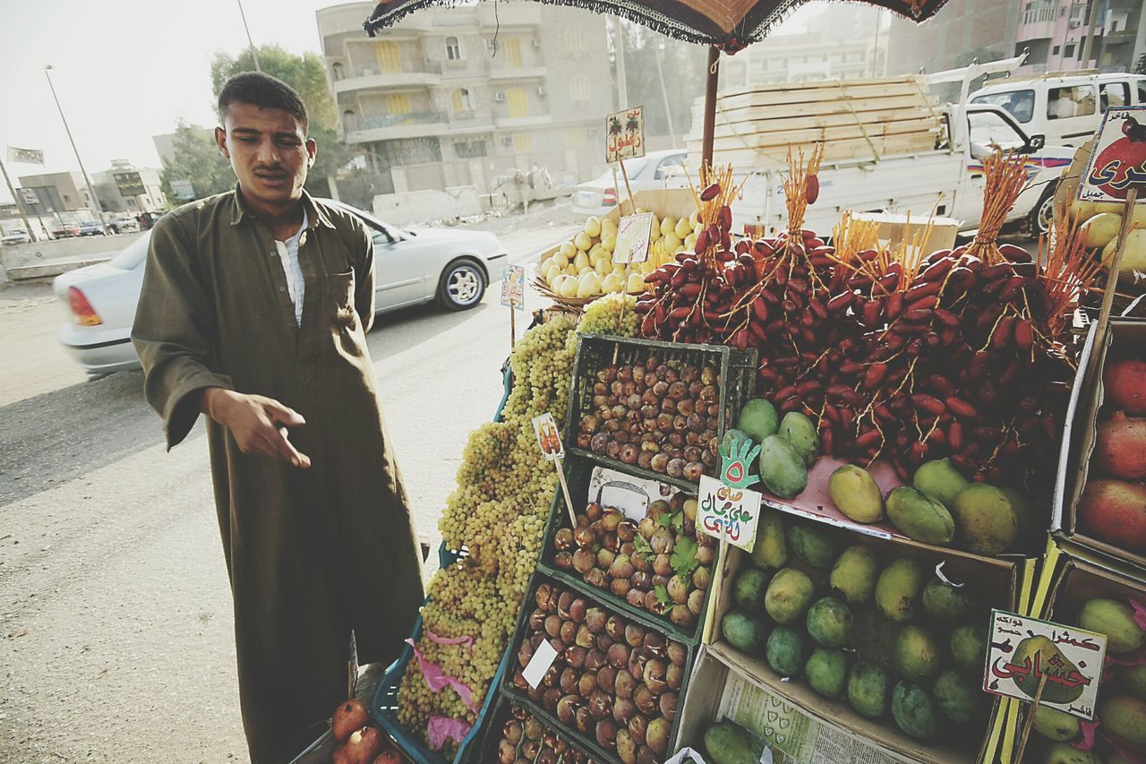 lifestyles, casual clothing, building exterior, leisure activity, men, food and drink, standing, retail, market, food, built structure, holding, architecture, young adult, street, market stall, young men, city