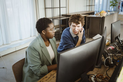 Multiracial programmers discussing over computer at desk in creative office