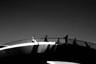 Low angle view of silhouette people perching on railing against clear sky