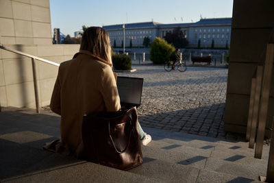 Woman sitting with a laptop on steps outdoors against sunset.