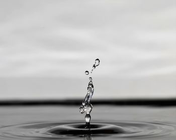 Close-up of drop falling on water against sky