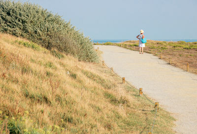 Woman walking on footpath against ocean