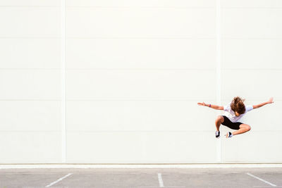 Full length of young man jumping on road against wall