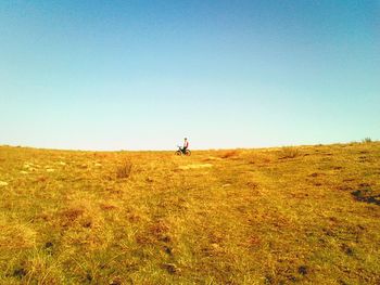 Mid distance view of man on bicycle at grassy field against clear blue sky