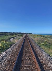 Empty railroad tracks against clear blue sky