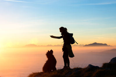 Low angle view of woman with arms raised against sky during sunset